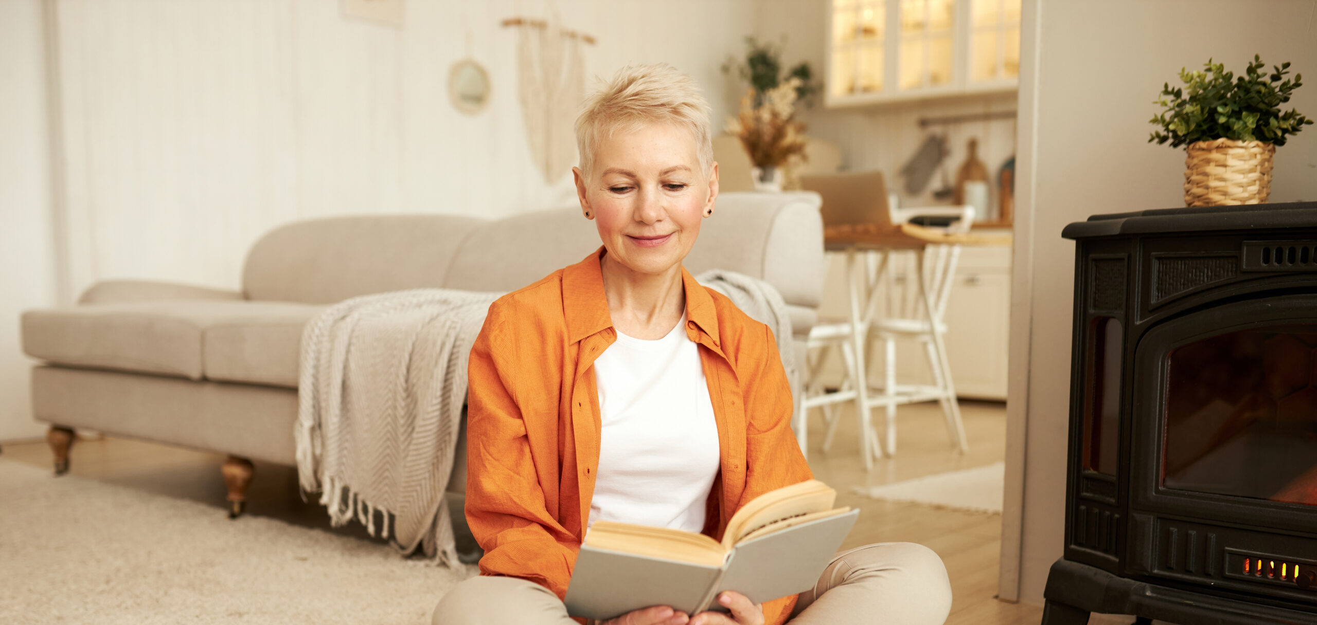 Mature smiling lady reading book by the fire at home